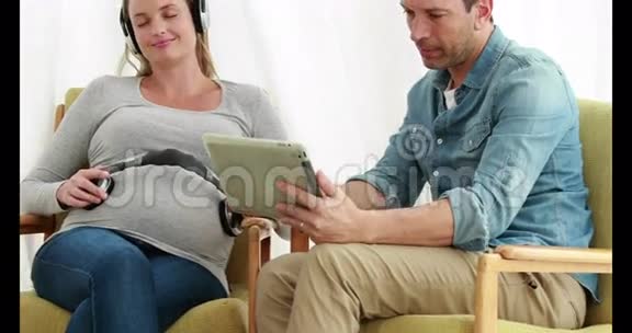 男人使用平板电脑而孕妇则听耳机音乐视频的预览图