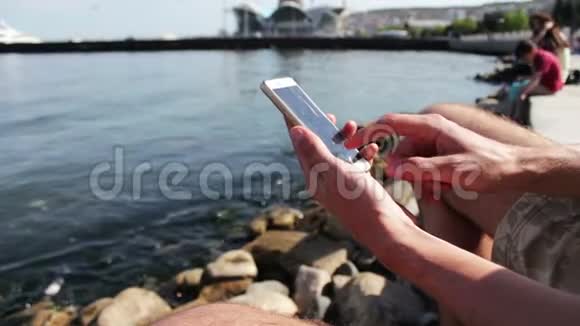 一个年轻人的手在里海的海浪背景下在智能手机上键入一些东西视频的预览图