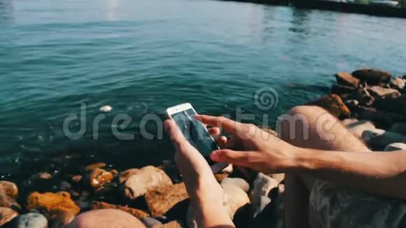 一个年轻人的手在里海的海浪背景下在智能手机上键入一些东西视频的预览图