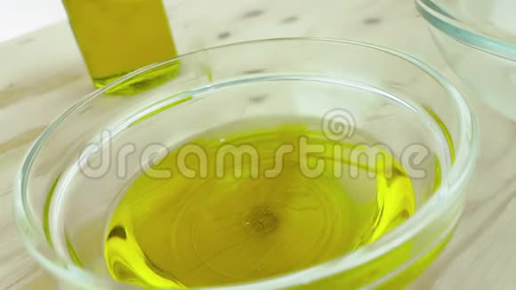 将煮好的橄榄油倒入白色容器中放在靠近橄榄油瓶的木桌背景上视频的预览图