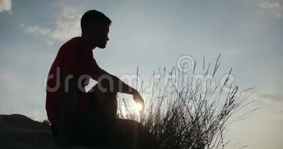 坐在悬崖边看日落的年轻人剪影视频的预览图