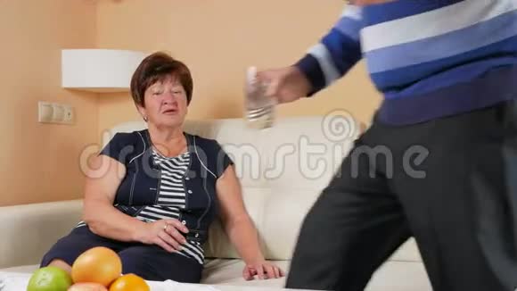 老人把带着一杯水的平板电脑带到家里的沙发上妇女健康状况不佳护理视频的预览图