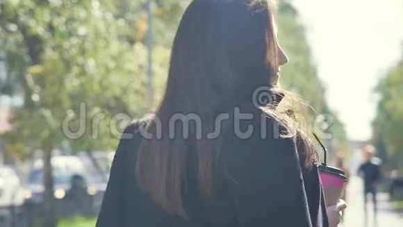 一个美丽快乐外表迷人的年轻女孩正拿着一杯咖啡走在城市的街道上视频的预览图