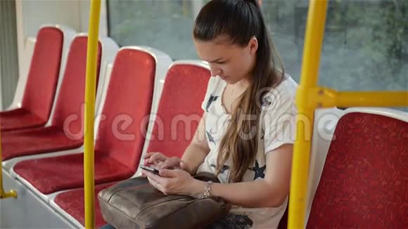 美丽的年轻女子乘坐城市交通工具使用她的手机女性在公共场合使用智能手机视频的预览图
