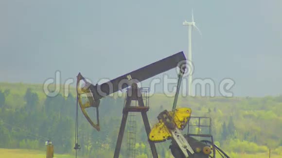 背景为灰色天空的油井抽油机和风力发电厂视频的预览图