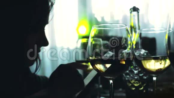 女人的剪影使用智能手机和一杯白葡萄酒坐在餐桌上3840x2160视频的预览图