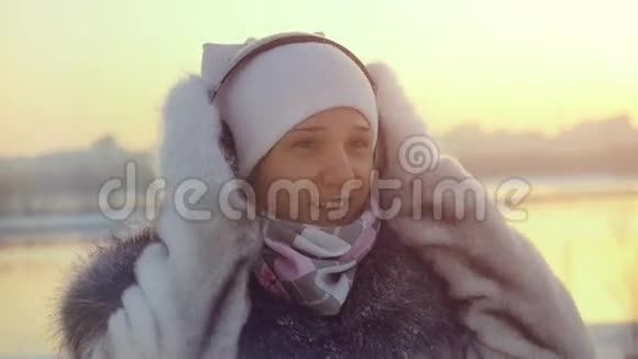 冬天的美丽女孩穿着冬天的衣服戴着耳机跳舞在日落时享受户外的慢动作视频的预览图
