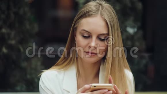 迷人的金发女人在她的智能手机上读到一些东西坐在咖啡馆的桌子旁视频的预览图