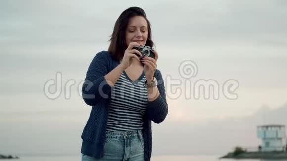 年轻女子在海边的老式相机上拍照一个有复古相机的女孩的肖像视频的预览图