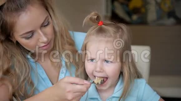 年轻的母亲用勺子喂她的孩子妈妈和女儿一起吃燕麦早餐视频的预览图