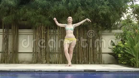 年轻苗条的女子在热带度假胜地的泳池边跳东方舞视频的预览图