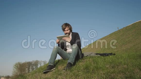 骑着平板电脑坐在公园草地上的帅哥视频的预览图