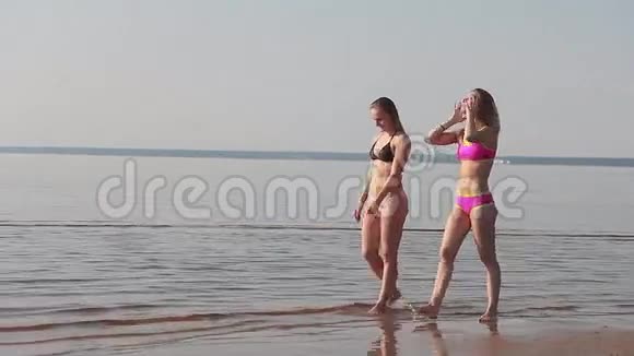 两个穿比基尼的年轻女孩在海滩散步视频的预览图