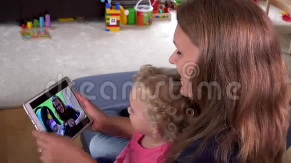 美丽的母亲和小女儿女孩在平板电脑屏幕上看家庭电影视频的预览图