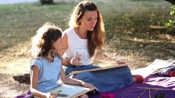 在阳光明媚的夏天年轻的女人在公园里教一个女孩画画视频的预览图