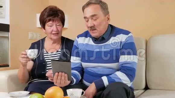 快乐的老两口热情地看着屏幕平板电脑和一杯茶丈夫和妻子视频的预览图