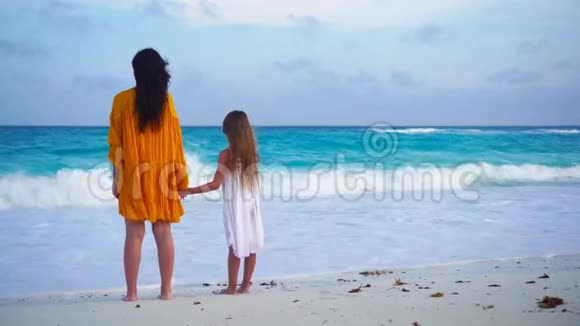 温暖的夜晚热带海滩上的小可爱女孩和年轻母亲视频的预览图