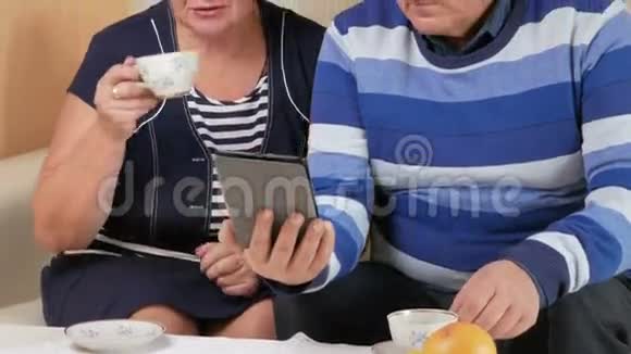 快乐的老两口热情地看着屏幕平板电脑和一杯茶丈夫和妻子视频的预览图