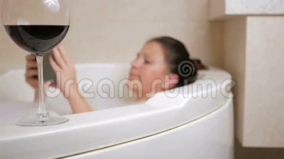 美丽的女孩洗澡与泡沫和平板电脑一个大白浴和一杯红酒盘子上的薄片视频的预览图