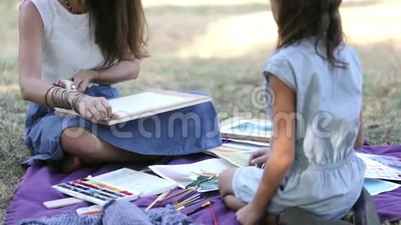 在阳光明媚的夏天年轻的女人在公园里教一个女孩画画视频的预览图