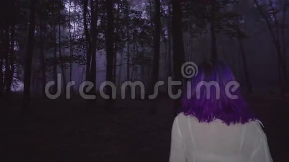 在黑暗森林中漫步的白色衬衫和紫色头发的美丽女人的后景惊悚的场景视频的预览图