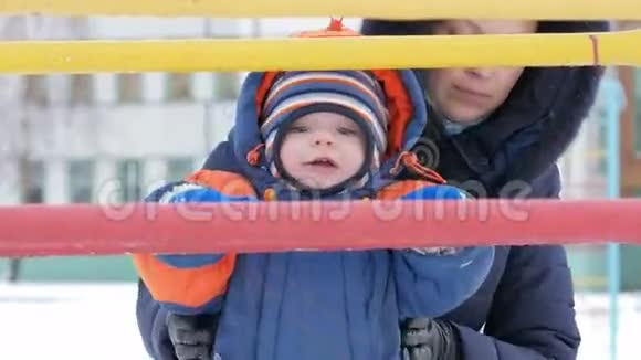 孩子冬天爬上金属山妈妈帮儿子男孩穿着工作服大约一年了冬季概念视频的预览图