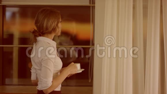 年轻女子站在窗前喝杯茶或咖啡视频的预览图