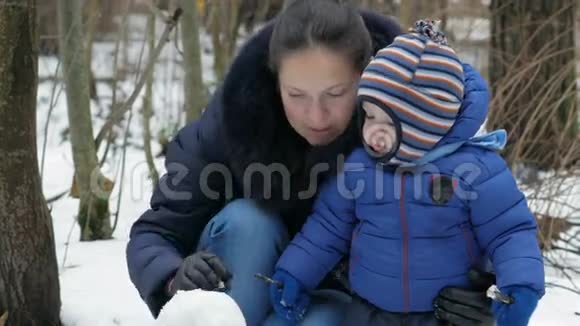 可爱的妈妈和宝宝在冬天的森林里雕刻小雪人圣诞假期的家庭乐趣视频的预览图