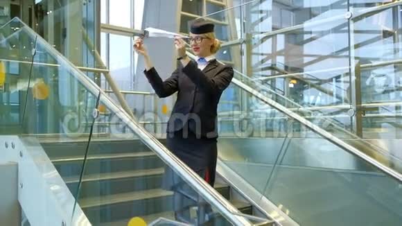 金发空姐站在楼梯上在大厅里做玩具纸飞机视频的预览图