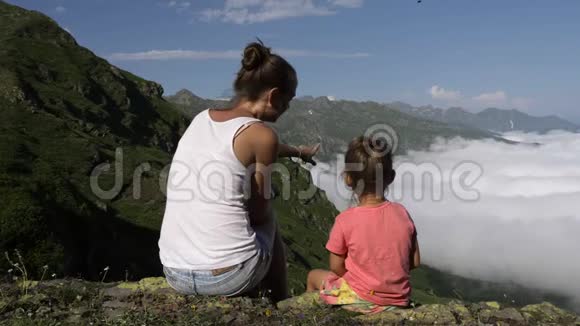 年轻的女人和小可爱的女儿坐在山顶上视频的预览图