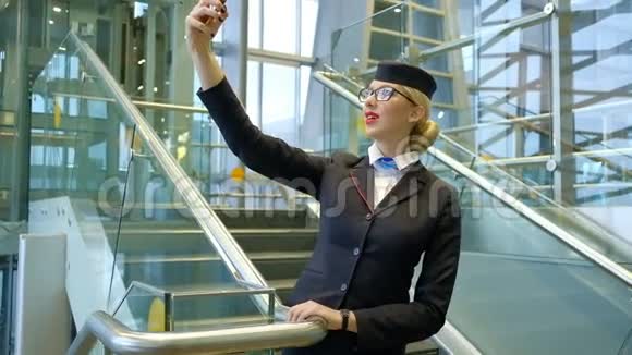 金发空姐站在楼梯上在智能手机上自拍视频的预览图