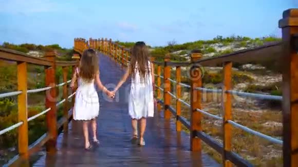 在去白色海滩和绿松石海洋的路上坐在木桥上的小孩子视频的预览图