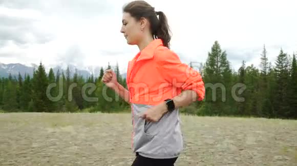 跑步者使用智能手表健身跟踪器和心率监视器在森林小径上慢跑女运动员检查视频的预览图