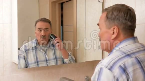 一个老人在浴室里刮电动剃须刀他照镜子仔细地剃掉她所有的头发它的叶子视频的预览图