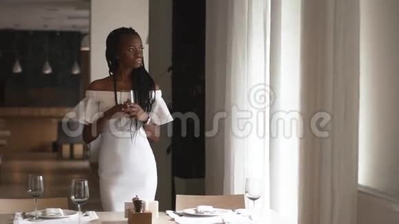 迷人的非裔美国女时装模特手里拿着空酒杯站在桌子旁边为视频的预览图