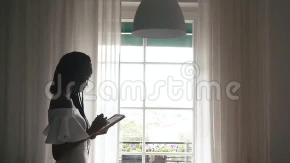 一位美丽的非洲女性时尚模特在阳光明媚的窗户背景下在平板电脑上打字的肖像视频的预览图