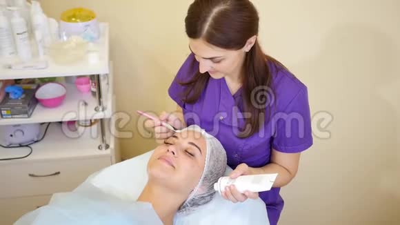 女人美容师把奶油面罩涂在脸上化妆程序视频的预览图