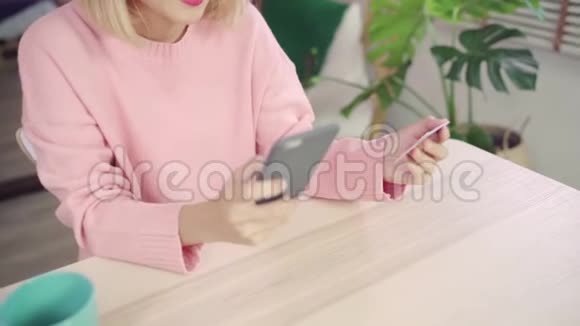 美丽的亚洲女人使用智能手机通过信用卡购买网上购物而穿毛衣坐在桌子上视频的预览图