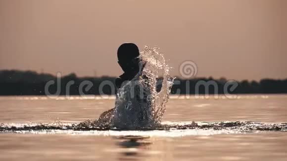 日落时快乐男孩的剪影用他的手创造水的飞溅慢动作视频的预览图