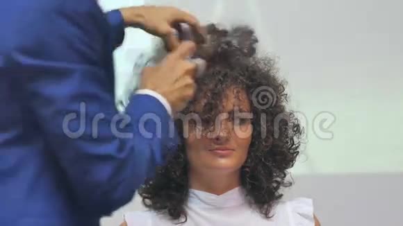 美容师在行动理发师做吹风机使卷曲的黑发变白舱里的金发理发师做头发视频的预览图