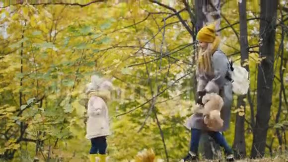 妈妈和她的女儿在秋天的公园里散步和泰迪熊玩耍视频的预览图