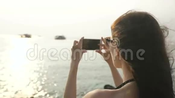 海滩岛上的女游客在船上度假时用智能手机拍摄日落和天际线景观视频的预览图