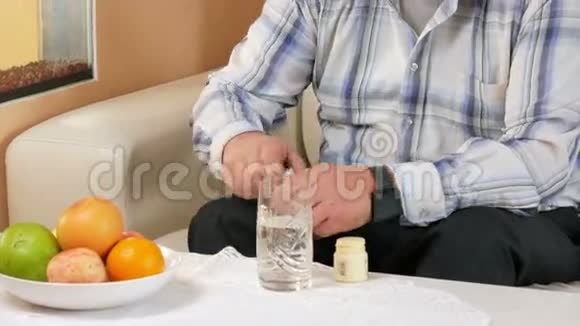老人胡子在家里吃药喝一杯水他坐在水族馆附近的沙发上视频的预览图