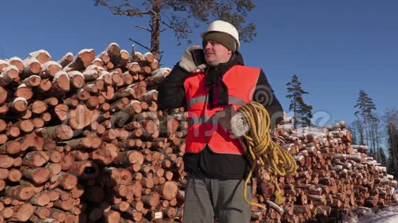 冬天在一堆木头附近用绳子和斧头打电话的伐木工人视频的预览图