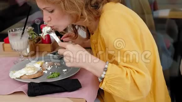 一位美丽的年轻女士在咖啡馆里用烤面包和鸡蛋吃早餐视频的预览图