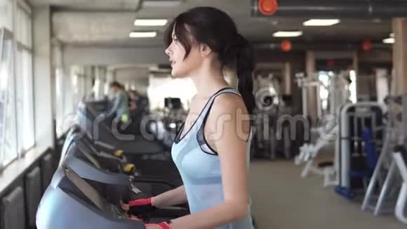 年轻女子在健身房的跑步机上行走健身房的有氧运动视频的预览图