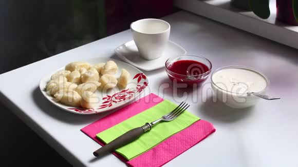 桌子上放着一盘慵懒的饺子热气从盘子里冒出来附近有酸奶油和果酱视频的预览图