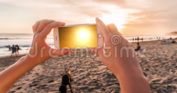 晚上女人用手机在海滩上拍摄日落拍摄时效性的电影视频的预览图