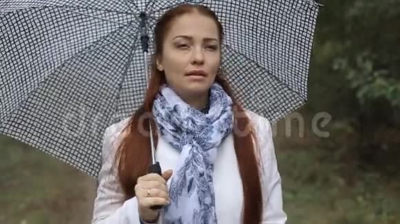 一位美丽的白人妇女一头红色的头发在一个阴天的秋天在公园里带着雨伞视频的预览图