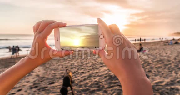 晚上女人用手机在海滩上拍摄日落拍摄时效性的电影视频的预览图